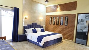 A bedroom with a large bed, a brick accent wall, and a sliding glass door to the bathroom. - Athulya Resort – Leisure and Luxury cottages from EMBEHolidays (Cheyyur)