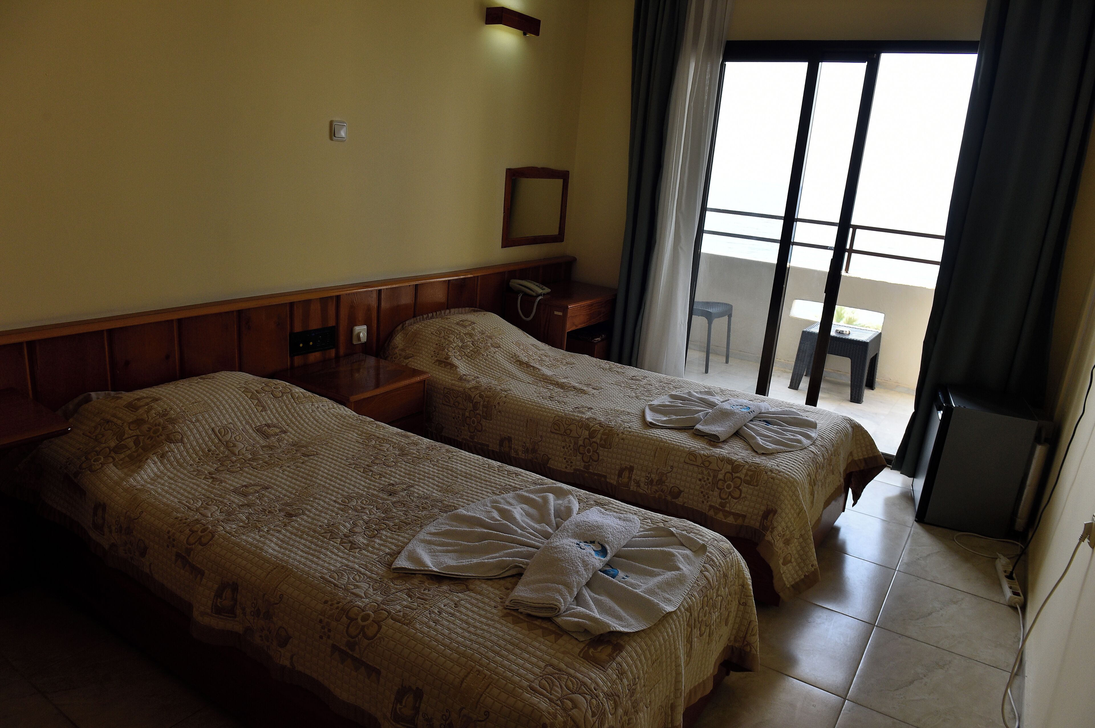 Habitación de hotel con dos camas, un escritorio, una silla, un teléfono y un balcón con vistas.