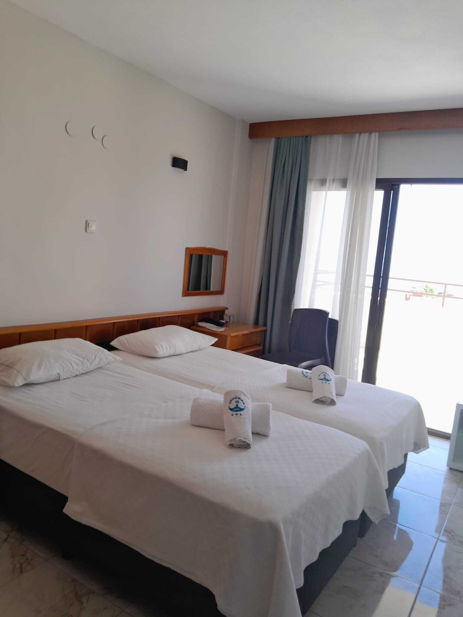 A hotel room with two beds, a nightstand, a chair, a mirror, and a view of the outdoors.