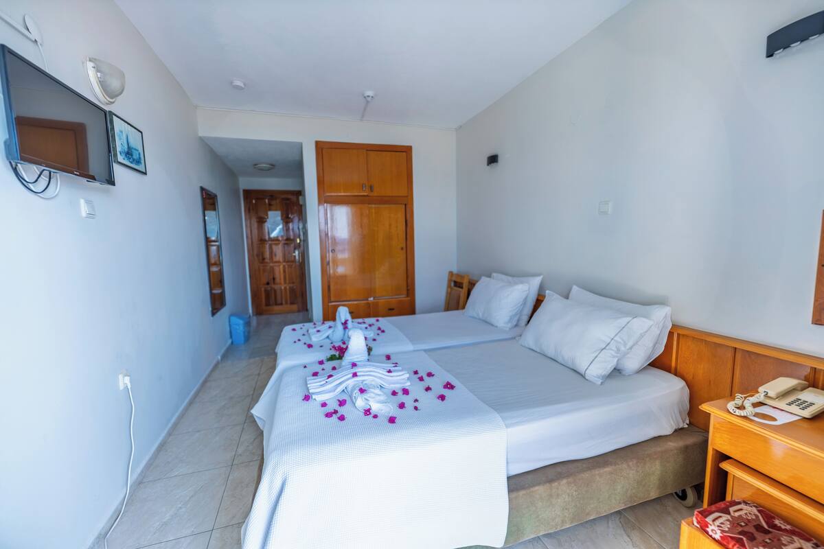 A hotel room with two beds, a wooden wardrobe, a bedside table with a phone, and a wall-mounted TV.