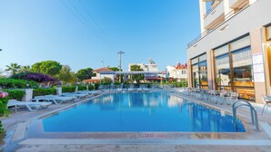 A swimming pool with lounge chairs and a building in the background. - Çidihan Hotel (Kuşadası)