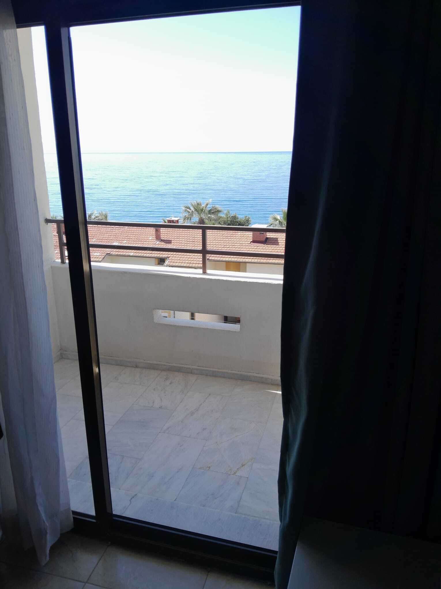 A room with a sliding glass door leading to a balcony with a view of the sea.