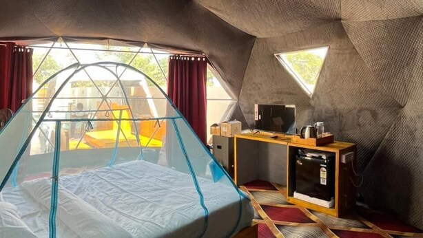 A compact, uniquely shaped room with a bed, a small table, and a television. - Infinity luxuria (Vikarabad)