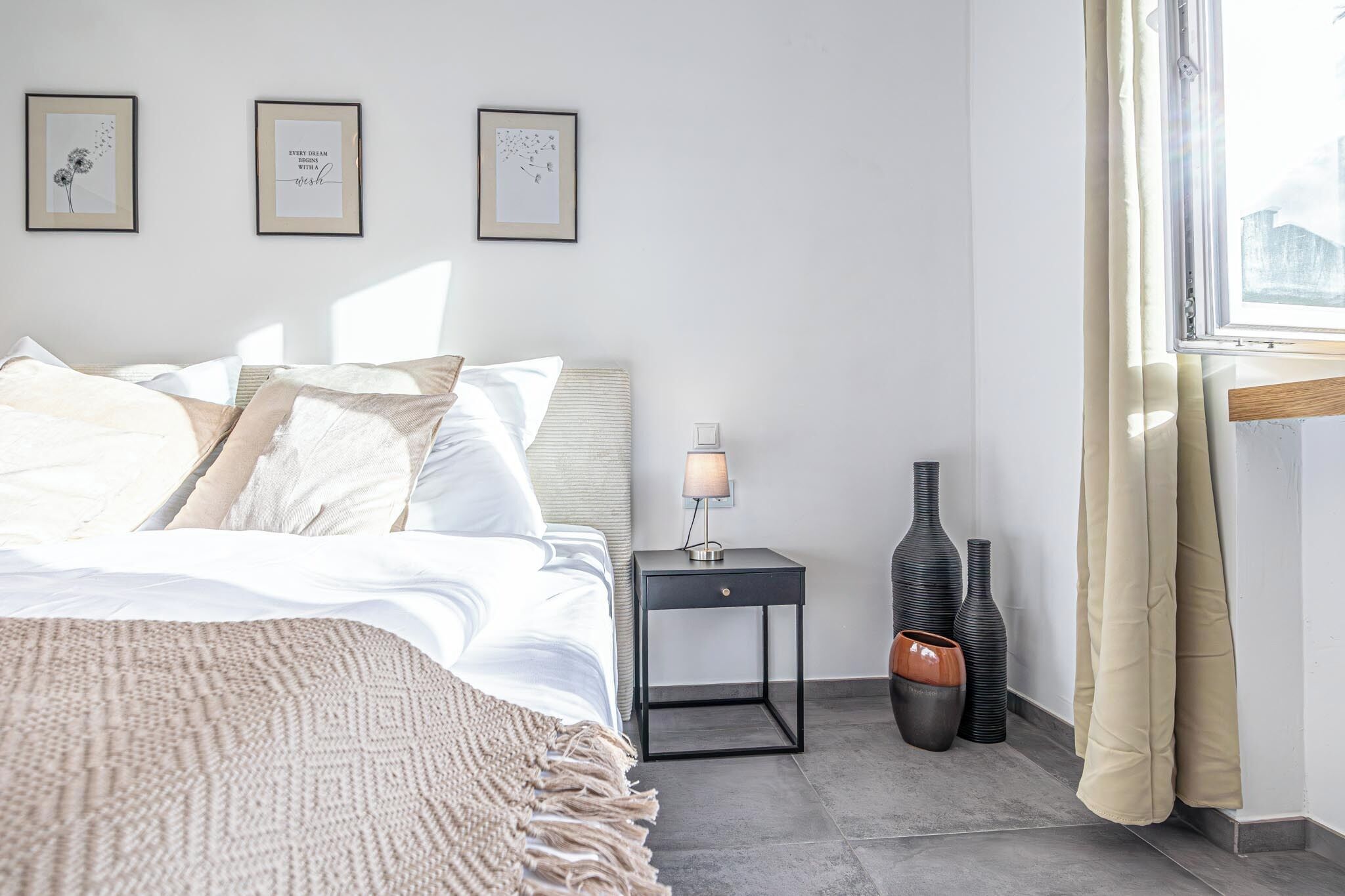 Un dormitorio ordenado con cama, mesita de noche, lámpara y jarrones decorativos.