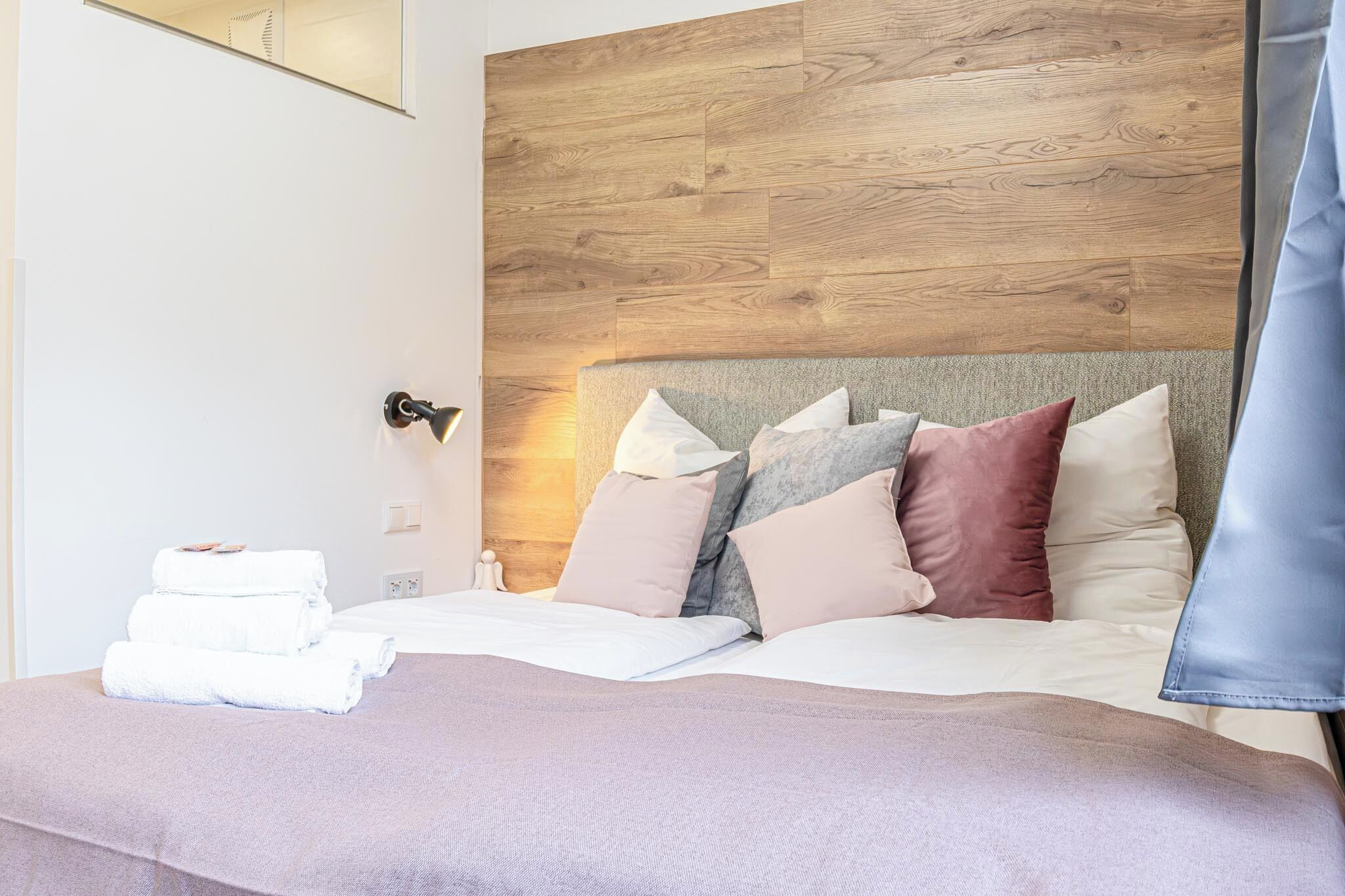 A neatly made bed with multiple pillows, a bedside table with a lamp, and a wooden headboard.