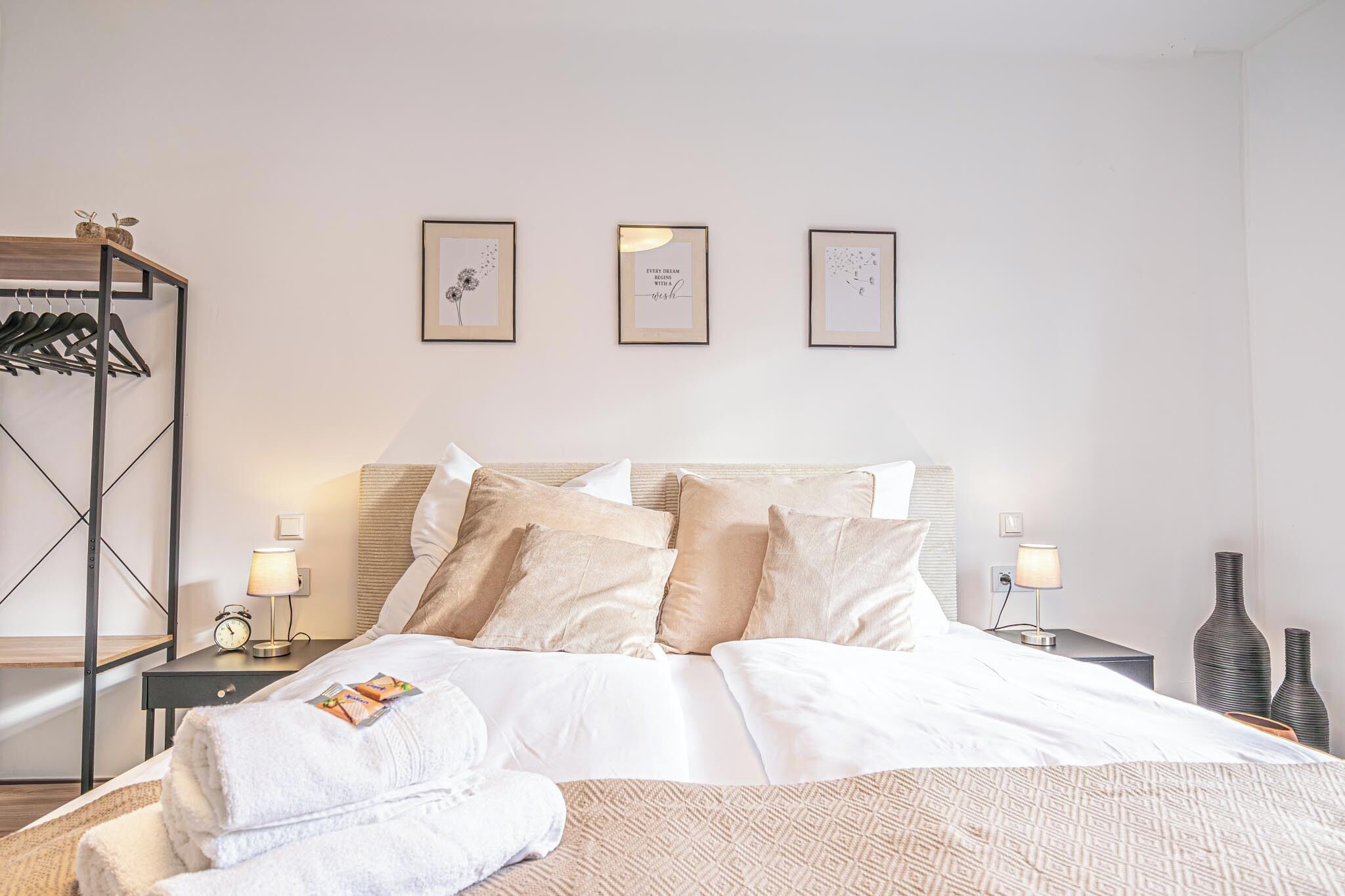 Une chambre d’hôtel bien rangée, avec un lit, des tables de chevet et un portant à vêtements.