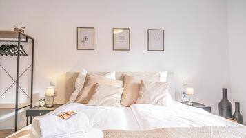 Une chambre d’hôtel bien rangée, avec un lit, des tables de chevet et un portant à vêtements.