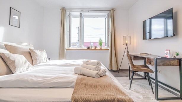 Een hotelkamer met een bed, bureau, stoel, televisie en raam met gordijnen.