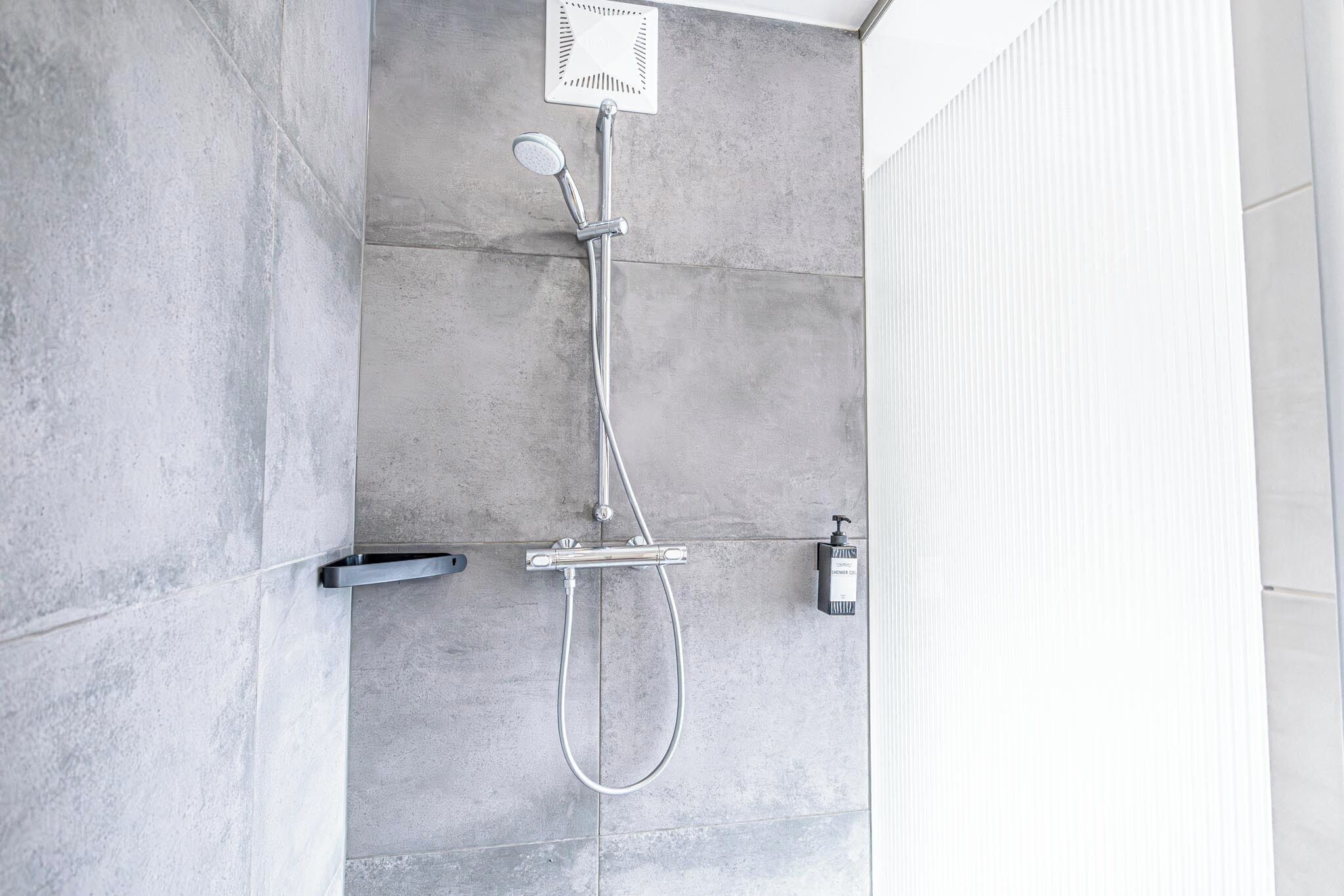 A modern shower with a handheld showerhead and a wall-mounted control panel.