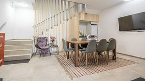 Een moderne eetruimte met een houten trap, een eettafel met stoelen en een flatscreen televisie aan de muur.