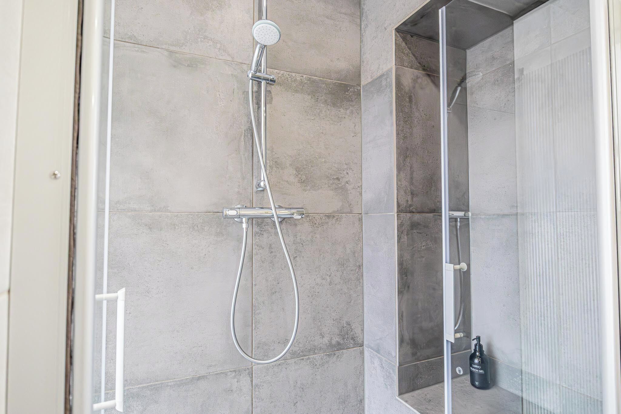 A modern shower with a handheld showerhead and a wall-mounted control panel.