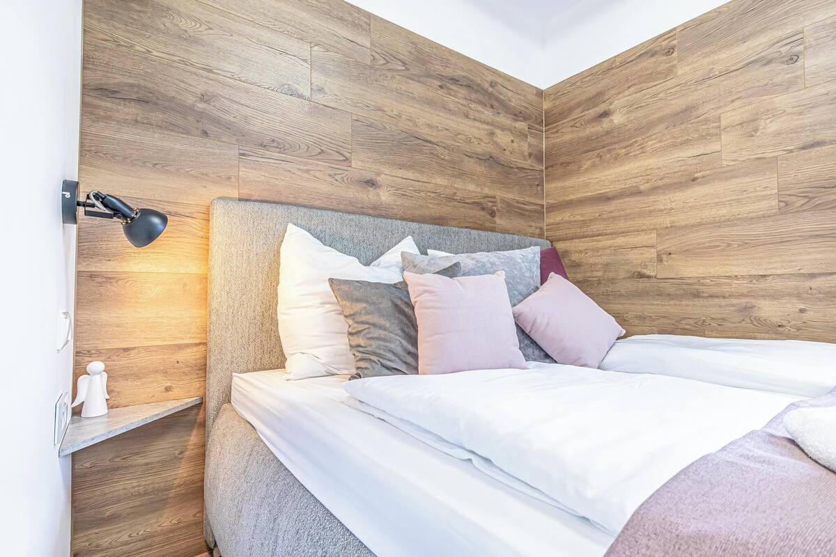Un dormitorio con cabecera de madera, lámpara de noche y cama con ropa blanca.