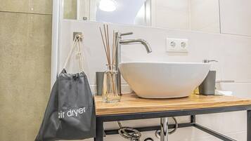 A bathroom with a white sink, a mirror, and a black bag hanging on the wall.