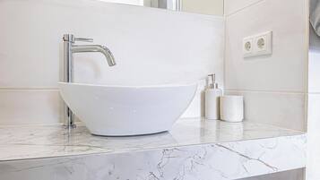 Ein Badezimmer mit einem weißen Haubenwaschbecken, einem chromfarbenen Wasserhahn und einer Marmorarbeitsplatte.