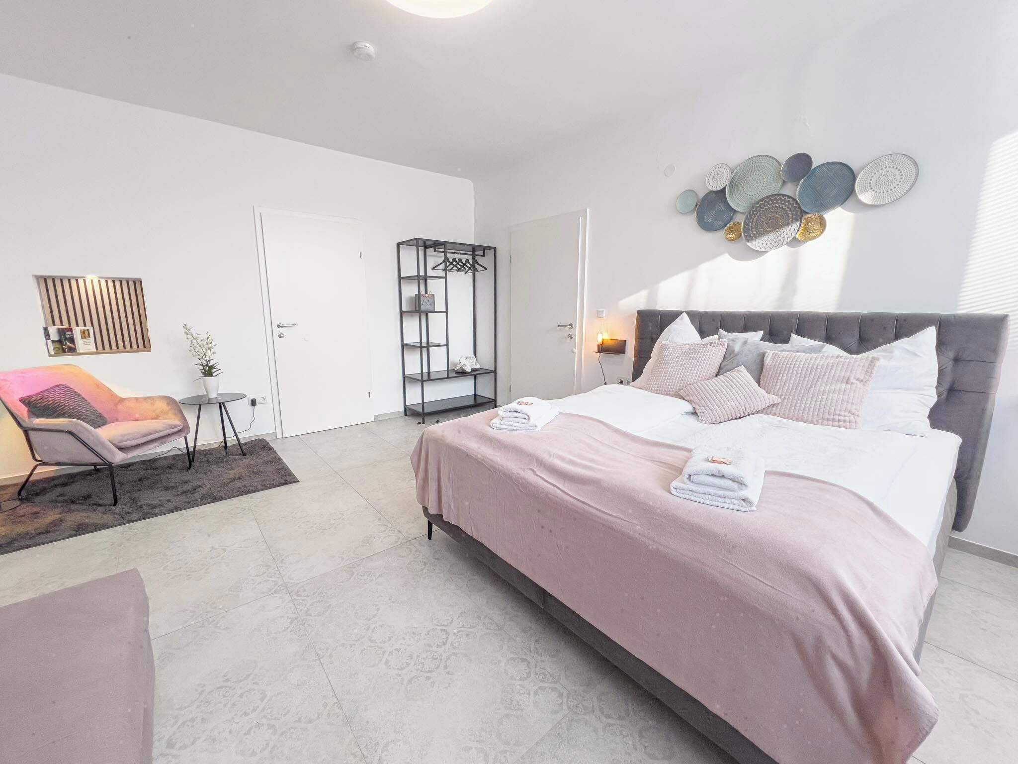 Een moderne slaapkamer met een groot bed, een zithoek met een stoel, een kleine tafel en een garderobe.