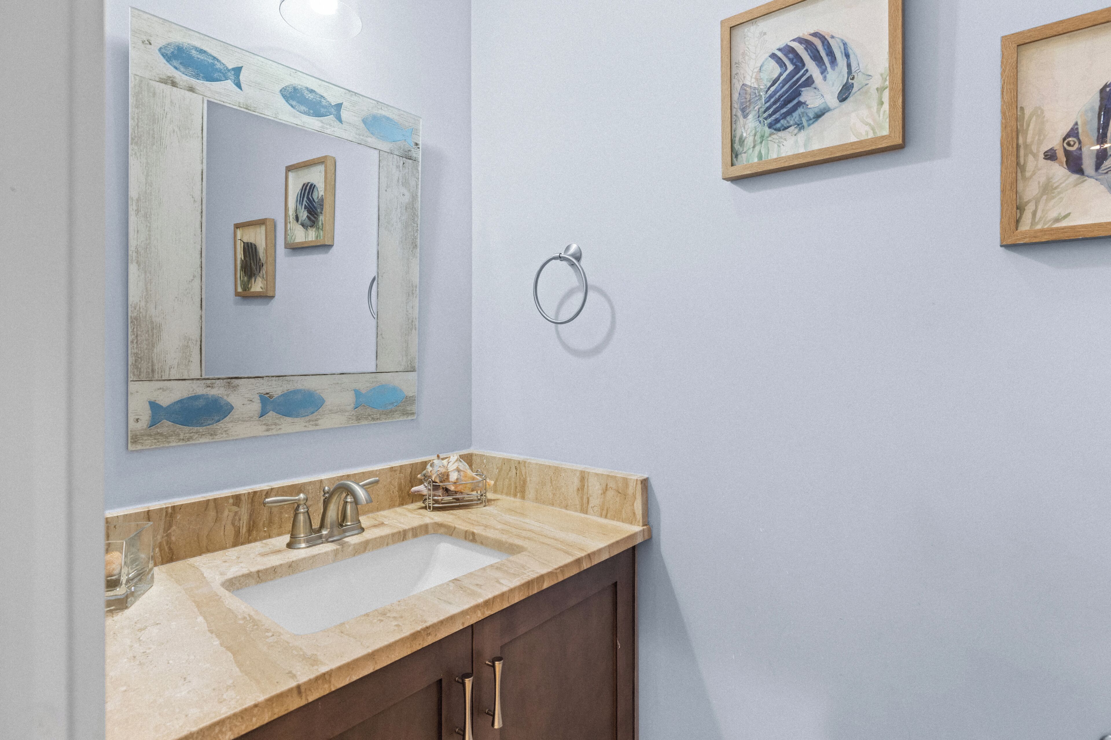 A bathroom with a wooden vanity, a sink, and a mirror. There are framed fish paintings on the wall.