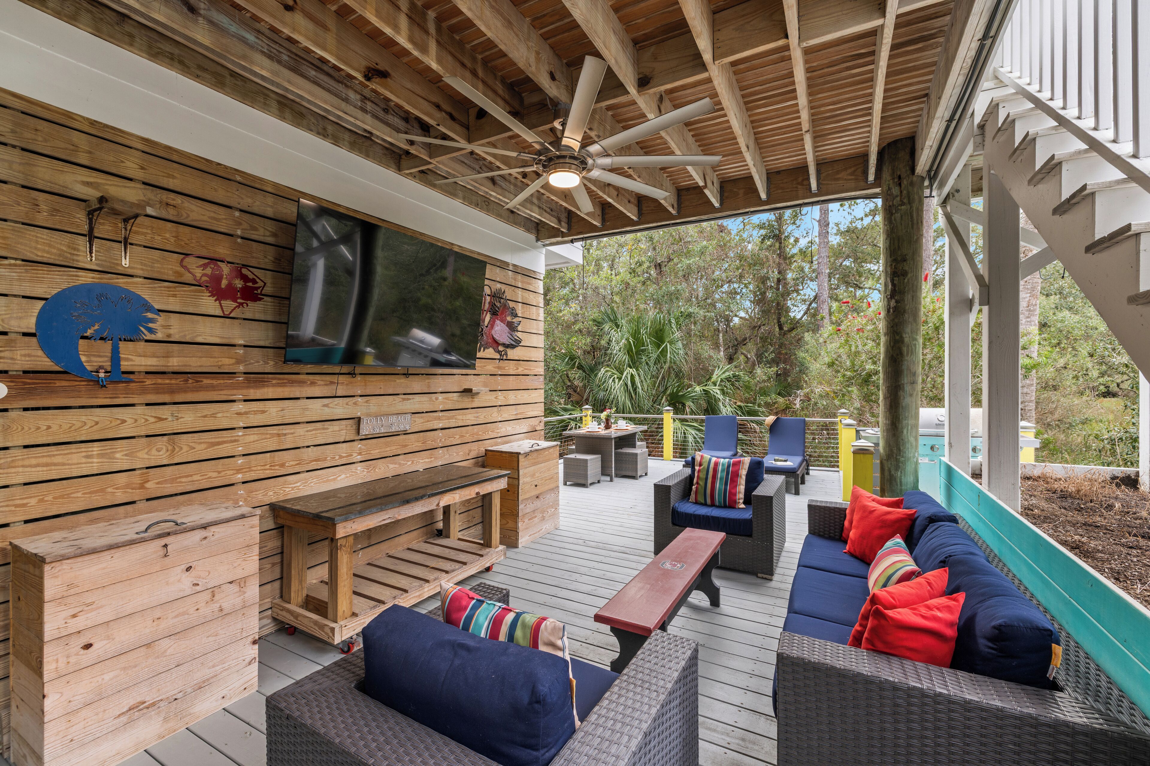 An outdoor deck with wooden furniture, a ceiling fan, and a view of the surrounding trees.
