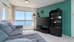 Un salon moderne avec un canapé d’angle gris, un téléviseur à écran plat, un meuble de rangement noir et une vue sur la mer.