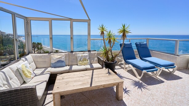 Un balcon avec un canapé blanc doté de coussins, une table en bois et deux fauteuils bleus.