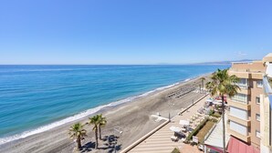Une vue sur la plage avec un hôtel, des palmiers et un ciel dégagé.