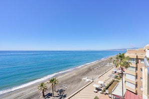Blick auf einen Strand mit Hotel, Palmen und blauem Himmel.