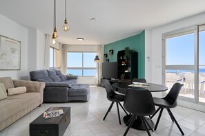 A modern living room with a sofa, a dining table with chairs, a TV, and a bookshelf. - Apartment 'Atico Alegria Del Mar By Immo Stoop' with Sea View, Rooftop Terrace, Pool (Málaga)