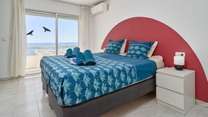 Une chambre à coucher avec un lit, une table de chevet, une fenêtre avec des rideaux et une vue sur la mer.
