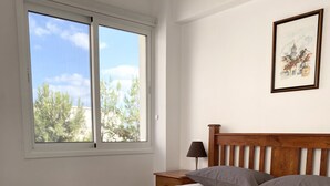 Una camera da letto con un letto grande, un comodino, una lampada, una finestra con vista sugli alberi e un quadro appeso al muro.