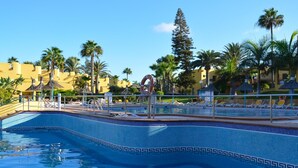 Una piscina con bordo decorato in piastrelle, circondata da lettini e palme.