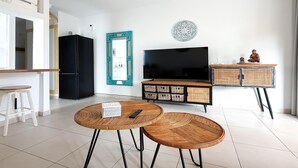 Un soggiorno moderno con una TV nera, uno specchio con cornice color acquamarina e un tavolino consolle in vimini.