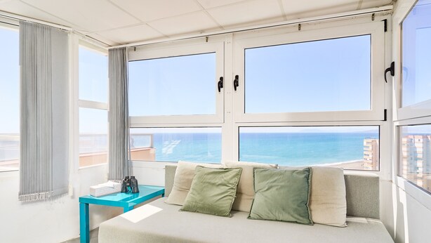 Ett rum med ett stort fönster, en soffa, ett litet bord och utsikt över havet.