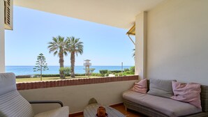 Un balcón con vista al mar, un sofá, una silla y una pequeña mesa con una vela.
