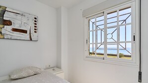 Un dormitorio con cama, mesita de noche, una obra de arte en la pared y ventana con vista al mar.