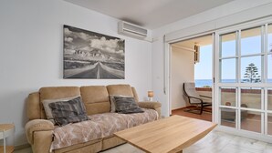 Una sala de estar con un sofá, una mesa de centro, un cuadro y vistas a través de una puerta de cristal.