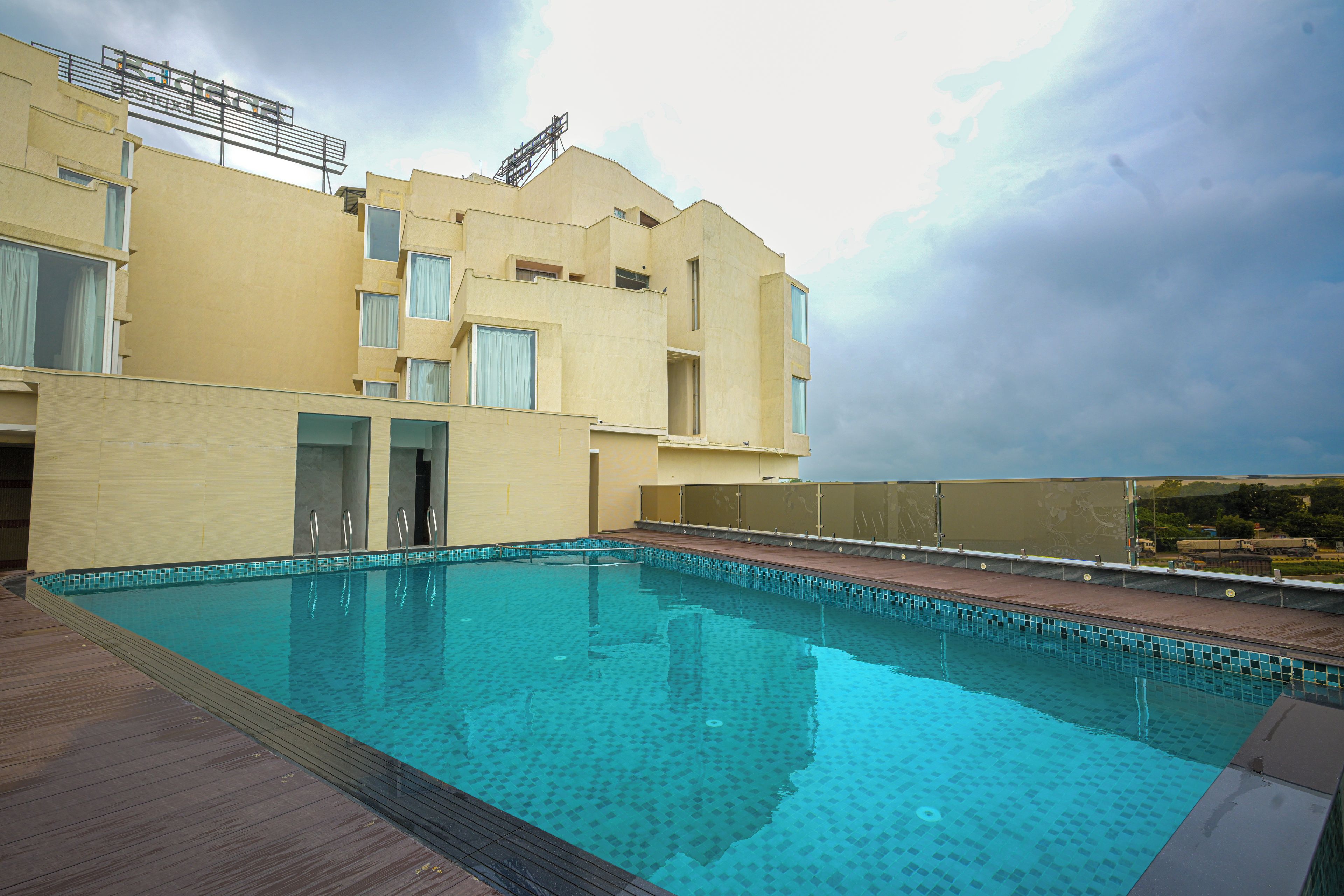 Piscina com deck de madeira, um edifício com várias janelas e céu nublado.