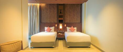 A hotel room with two beds, a nightstand, a lamp, a sofa, and a magazine on a table.