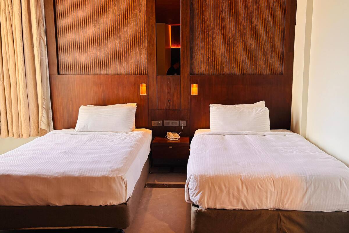 A hotel room with two beds, wooden paneling on the walls, and a nightstand with a telephone.