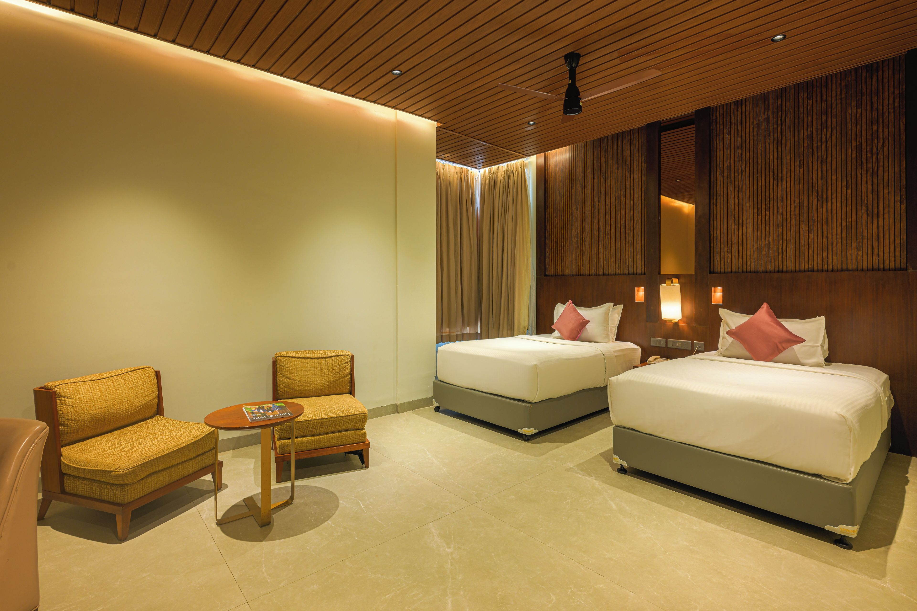 Ein Hotelzimmer mit zwei Betten, einem Schlafsofa, einem kleinen Tisch und einem Deckenventilator.