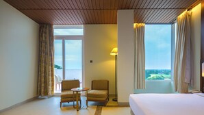 Une chambre d’hôtel avec un lit, deux chaises, une petite table, une lampe sur pied et une vue sur l’extérieur.