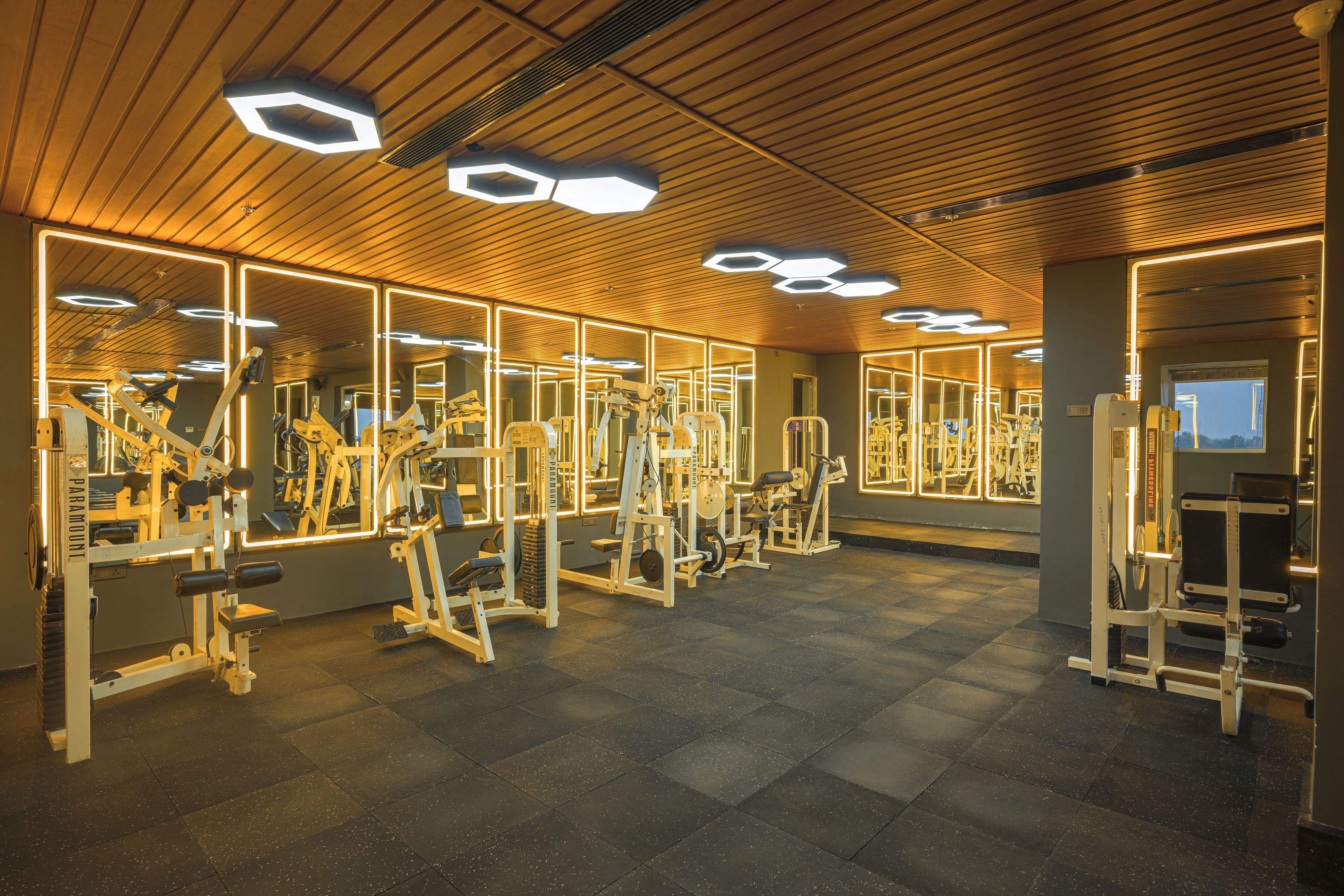 A gym with mirrored walls, exercise equipment, and hexagonal ceiling lights.