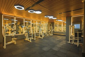 Un gimnasio con paredes espejadas, equipo de ejercicio e iluminación de techo hexagonal.
