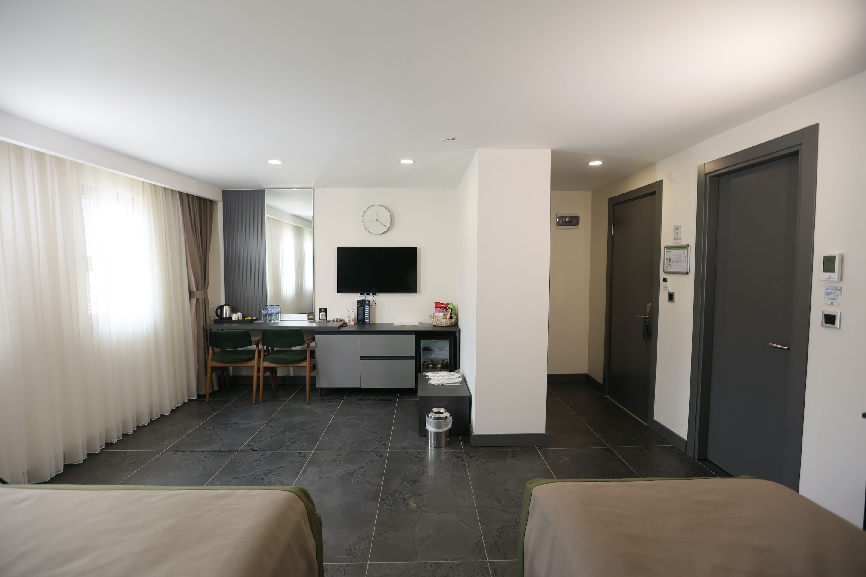 A hotel room with a bed, a desk, a chair, a TV, and a door.