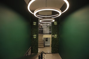 Un interior modern amb lluminàries circulars, una escala i detalls de paret verds.