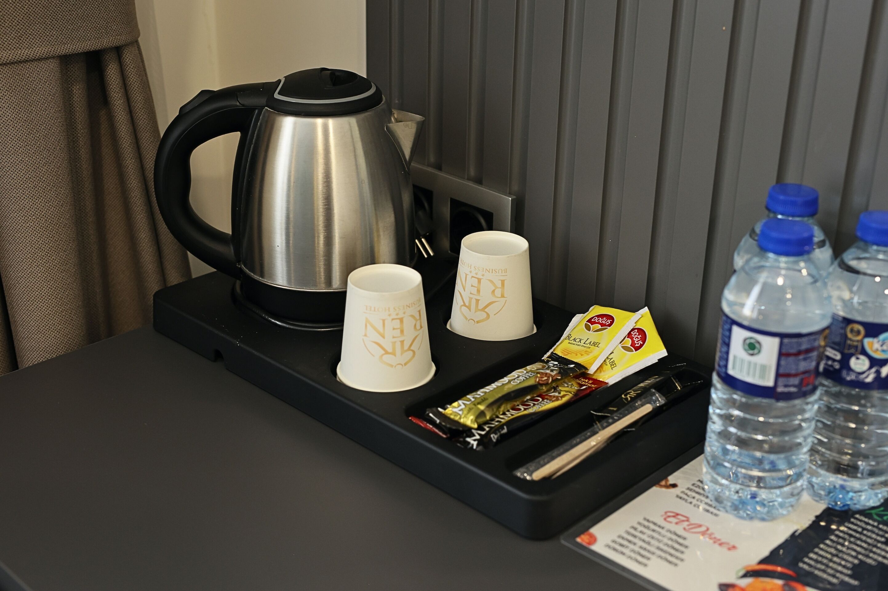 A hotel room with a coffee maker, two cups, a tray with snacks, and bottled water.