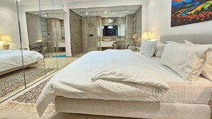 Ein modernes Schlafzimmer mit einem großen Bett, einer Duschkabine aus Glas, einer Sitzecke mit einem Sessel und einem Gemälde an der Wand.