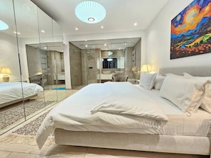 Een moderne hotelkamer met een groot bed, een douche met glazen wanden, een zithoek en een schilderij aan de muur.