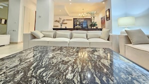Ein modernes Wohnzimmer mit einem großen Marmortisch, einem beigefarbenen Sofa und einem Essbereich mit einer Chandelier.