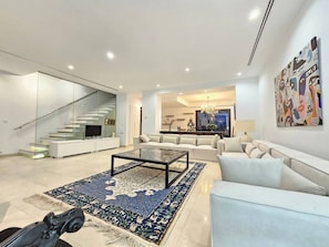 Una sala de estar moderna con una escalera de cristal, un conjunto de sofás, una mesa de centro y una alfombra estampada.