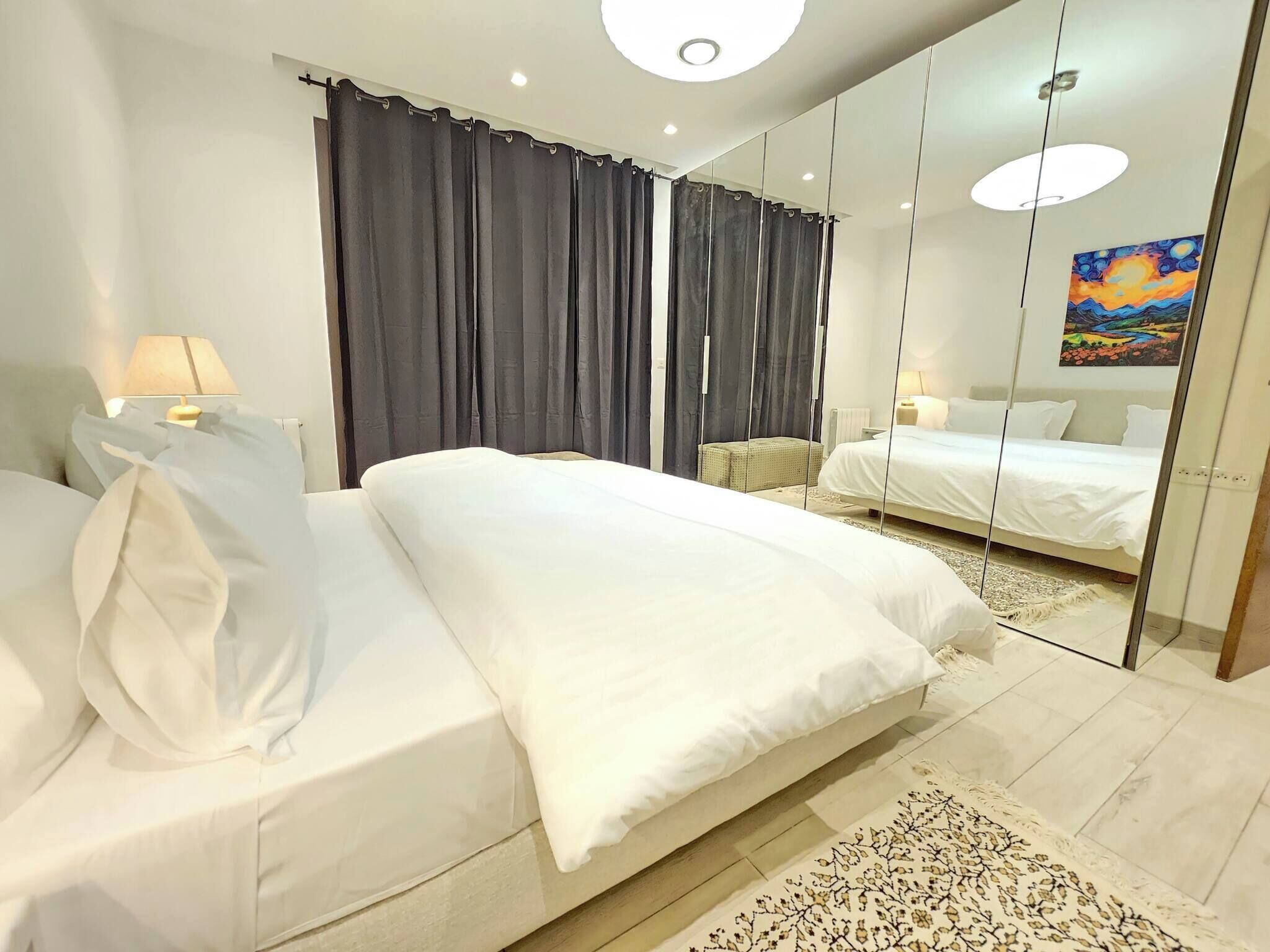 Un dormitorio moderno con una cama grande, un pequeño rincón de descanso y un espejo que refleja la habitación.