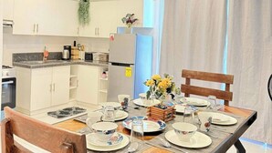 Moderni keittiö, jossa on valkoiset kaapit, ruokapöytä, jonka päällä on lautasia, kuppeja ja koristeellinen pöytäkoriste.